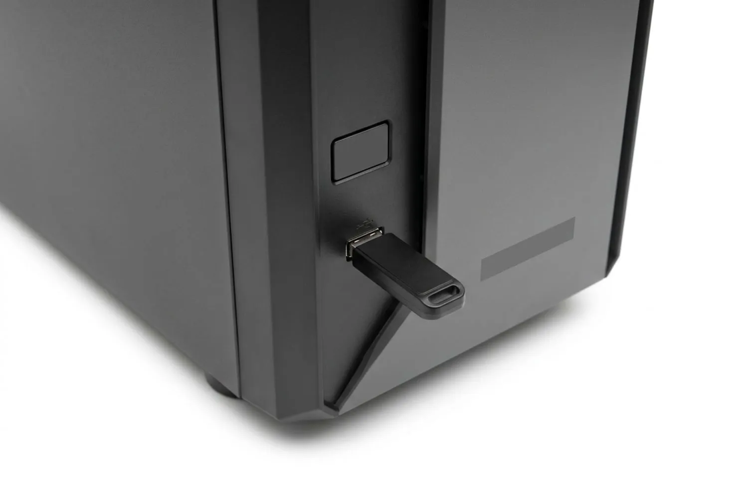 A small black USB flash drive plugged into the front panel of a dark PC case, lit from one side, with the case’s power button just above it
